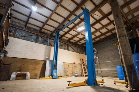 Hoist set up in workshop shed for machinery maintenance with concrete floor and repaired roof