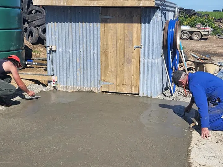 Construction workers smoothing concrete area outside shed