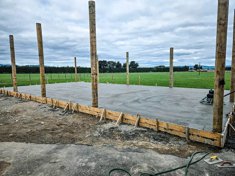 Concrete floor getting smoothed for a garage pole shed, with poles secured in the concrete