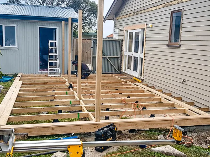 Builders working on a deck patio between house and garage, workers framing up the timber