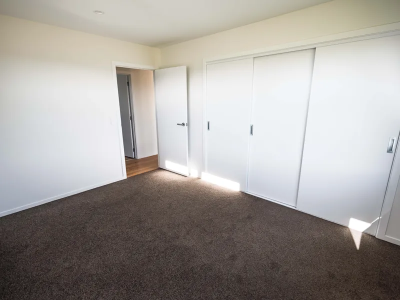 Guest bedroom of a new house with dark grey carpet and white walls, large wardrobe