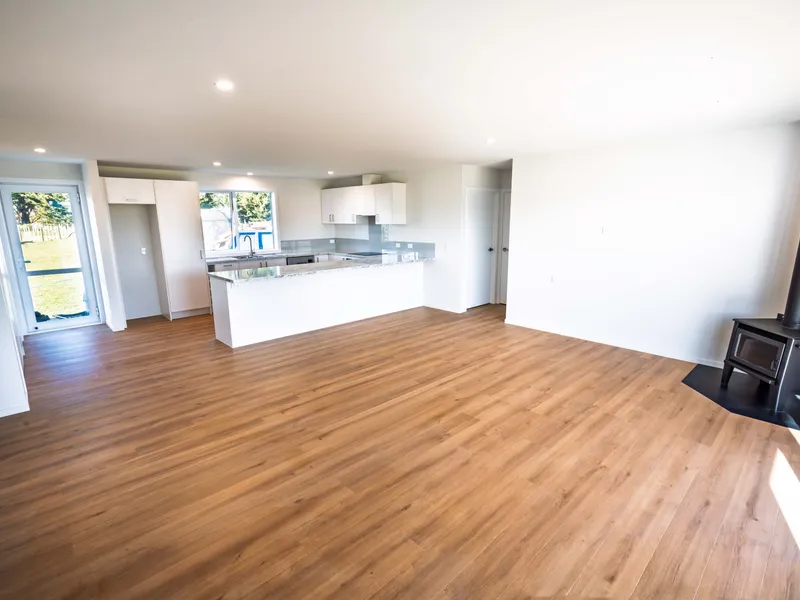 Lounge of a new house, with open plan kitchen and fireplace and wooden