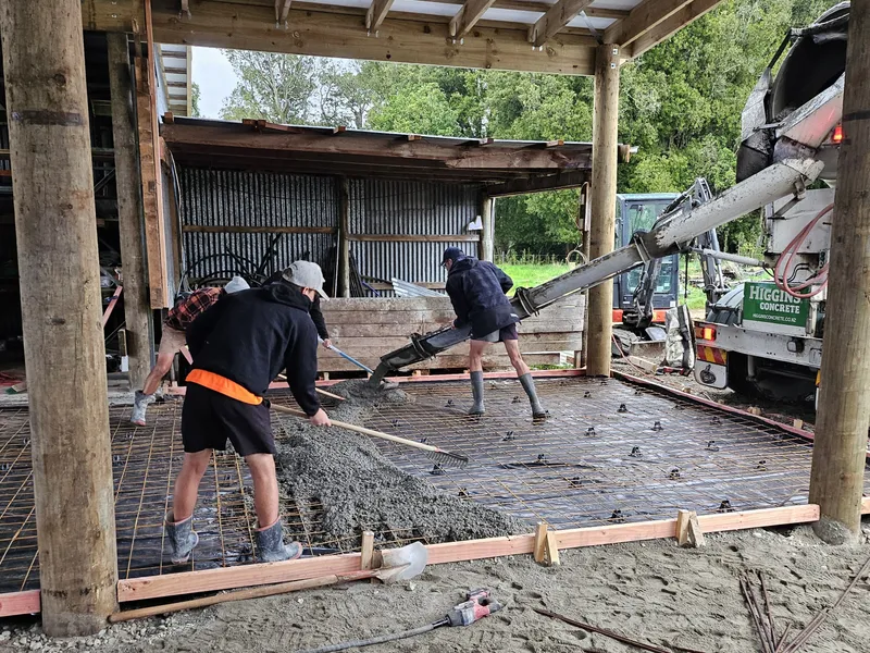 Construction workers pouring concrete for a concrete floor in a farm workshop